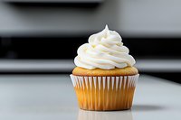 Vanilla cupcake with swirled white buttercream frosting on light surface against blurred background, classic bakery dessert for celebrations and events.