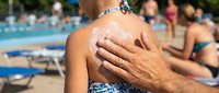 Adult male applying sunscreen lotion to young boy's shoulder at outdoor swimming pool on sunny day, sun protection and family beach safety concept.
