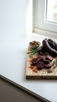 Artisanal charcuterie board with sliced salami, olives and herbs on wooden cutting board by bright kitchen window for gourmet cooking and food styling.