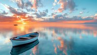 Wooden boat floating on calm water at sunset with dramatic orange and pink clouds reflected in tranquil sea surface, creating serene seascape atmosphere.