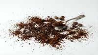 Ground coffee powder scattered on white surface with metal measuring spoon, suitable for beverage, food, and culinary design projects.