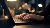 Hands typing on laptop keyboard in warm evening light with bokeh background creating cozy workspace atmosphere for productivity and remote work.