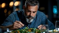 Mature bearded man enjoying healthy salad meal at restaurant with warm ambient lighting and bokeh background for dining concepts.