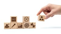 Hand placing wooden cube with teamwork icon completing business strategy concept with goal target growth puzzle symbols on white background.