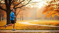 Young athletic woman jogging in autumn park during golden hour sunrise with warm sunlight filtering through colorful fall foliage trees.