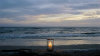 Glowing lantern on sandy beach at twilight with ocean waves and dramatic cloudy sky creating peaceful coastal atmosphere for relaxation and meditation.