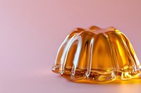 Orange jelly dessert with ridged shape on pink background, translucent gelatin wobbling with glossy surface catching light and creating shadows.
