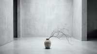 Minimalist still life with dried plant emerging from ceramic vessel in empty concrete room with architectural columns and neutral tones.