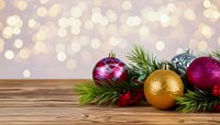 Festive Christmas decoration with gold and pink baubles, pine branches on wooden table against blurred bokeh background.