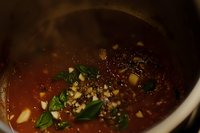 Homemade tomato sauce simmering in pot with fresh herbs, garlic, and spices. Close-up view shows rich red color and aromatic ingredients creating depth of flavor.