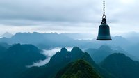 Ancient bronze bell hanging over misty mountain peaks at sunrise, dramatic foggy valleys between green ridges create mystical Asian landscape atmosphere.