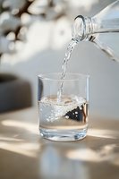Fresh water pouring from glass bottle into transparent drinking glass with dynamic splash and natural sunlight creating soft shadows on table surface.