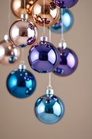 Shiny Christmas ornaments in rose gold, purple and turquoise blue hanging against neutral background create modern festive holiday decoration arrangement.