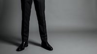 Cropped view of person wearing black formal trousers and polished dress shoes, standing against neutral gray background for corporate and professional styling concepts.