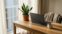 Cozy home office workspace with laptop, coffee cup and snake plant on wooden desk near window for remote work and productivity.