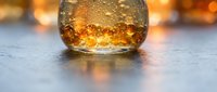 Glass of whiskey with ice cubes on reflective surface with warm bokeh lighting in background, suitable for beverage, alcohol, and hospitality design projects.