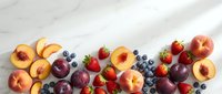 Fresh summer fruits including peaches, plums, strawberries and blueberries arranged on white marble surface for healthy eating and nutrition concepts.