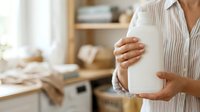 Unrecognizable woman in striped shirt holding blank white container in bright kitchen, suitable for product mockups, packaging design, and household product advertising.