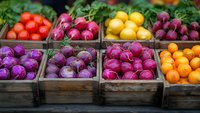 Fresh organic produce in rustic wooden crates at farmers market featuring vibrant purple and red beets, yellow lemons, tomatoes and radishes arranged in rows.