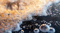 Ocean wave foam bubbles on sandy beach shore with golden sunlight creating sparkling water droplets and sea spray during sunset or sunrise coastal scene.