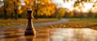 Wooden chess king piece standing alone on chessboard in autumn park with golden foliage background. Strategic thinking and leadership concept for business.
