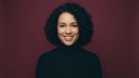 Happy young African American woman with curly hair smiling warmly in black turtleneck against burgundy background for professional headshot photography.