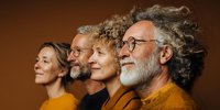 Diverse group of senior adults with gray hair and glasses in profile against warm brown background, showcasing aging with confidence.