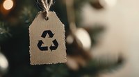 Recycling symbol on kraft paper tag hanging against blurred Christmas tree background with bokeh lights, eco-friendly holiday concept.
