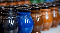 Colorful ceramic pots in row showing gradient from dark to bright blue and brown, handcrafted pottery vessels with decorative rims and glazed finish.
