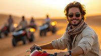 Young Caucasian man with sunglasses and scarf smiling while riding quad bike in desert during golden sunset, group of ATV riders in background enjoying adventure tour.