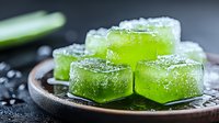 Green jelly cubes with sugar coating on dark ceramic plate, macro food photography with selective focus and water drops, fresh dessert.