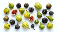 Fresh figs collection with green and purple varieties scattered on white background, some cut open showing red flesh, perfect for culinary designs.