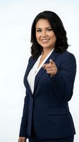 Confident Latina businesswoman in navy suit pointing at camera, smiling on white background, isolated for corporate and marketing use.