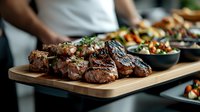 Grilled beef medallions with herbs on wooden serving board, accompanied by roasted vegetables in dark bowls, restaurant food presentation style.