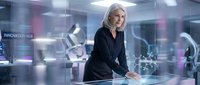 Mature woman with white hair in professional black blazer working at futuristic digital interface with holographic displays in modern tech office environment.