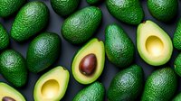 Fresh ripe green avocados arranged on dark background with two halved avocados showing creamy flesh and pit, top view composition for healthy food and cooking concepts.