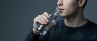 Young adult male of Caucasian ethnicity drinking water from a bottle against neutral gray background, suitable for health, wellness, fitness and hydration lifestyle content.
