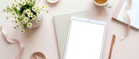 Feminine workspace flat lay with white tablet, chamomile flowers, coffee cup and rose gold accessories on blush pink background for branding mockup.