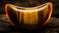 Golden tiger eye gemstone bowl with natural striped patterns and warm amber glow on dark wooden surface for meditation and healing crystal collection.
