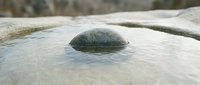 Smooth river stone partially submerged in clear shallow water with natural rock formations creating peaceful zen-like scene for meditation and relaxation.