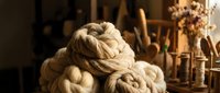 Natural wool yarn skeins in rustic workshop setting with wooden tools and dried flowers creating cozy handcraft atmosphere for knitting projects.