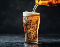 Golden beer pouring from bottle into pint glass with rising bubbles and frothy head against dark background, capturing dynamic flow and carbonation in dramatic lighting.