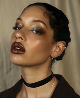 Young mixed race woman with glamorous evening makeup, dark burgundy lips, smokey eyes, and finger waves hairstyle wearing black choker necklace against neutral background.