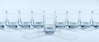 Clear glass tumbler standing out from row of empty glasses on white surface. Minimalist glassware concept for beverage service and hospitality industry.