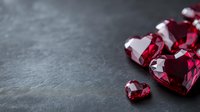 Red heart shaped gemstones scattered on dark stone background with copy space, romantic luxury jewelry concept for Valentine's day or anniversary gift.