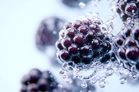 Fresh blackberries covered in sparkling water bubbles against light blue background, macro photography showing detailed texture and reflections.