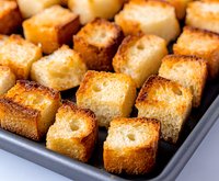 Golden brown homemade croutons arranged on dark baking sheet, crispy bread cubes with toasted edges showing texture and crunch, ready for salads and soups.