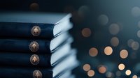 Stack of navy blue hardcover books with gold embossed compass design on spines against dark background with soft bokeh lights creating magical atmosphere.