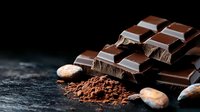 Dark chocolate bar pieces with cocoa powder and cocoa beans on black stone background, dramatic lighting creates luxurious mood for food photography.