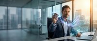 Businessman in office analyzing financial data with holographic charts and graphs displayed on screen during sunset cityscape view.